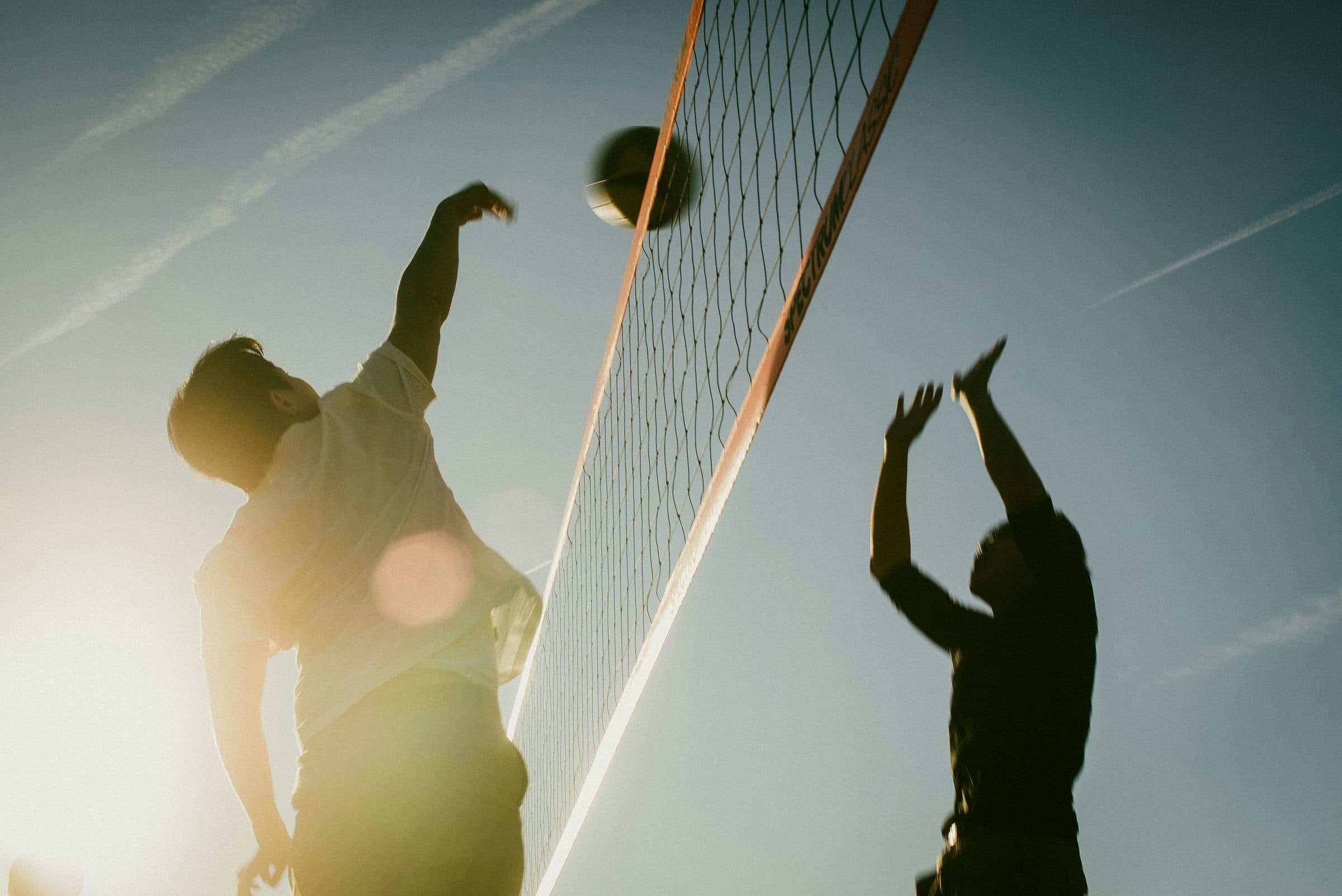 Jugadores de voleibol playa saltando en la red al atardecer
