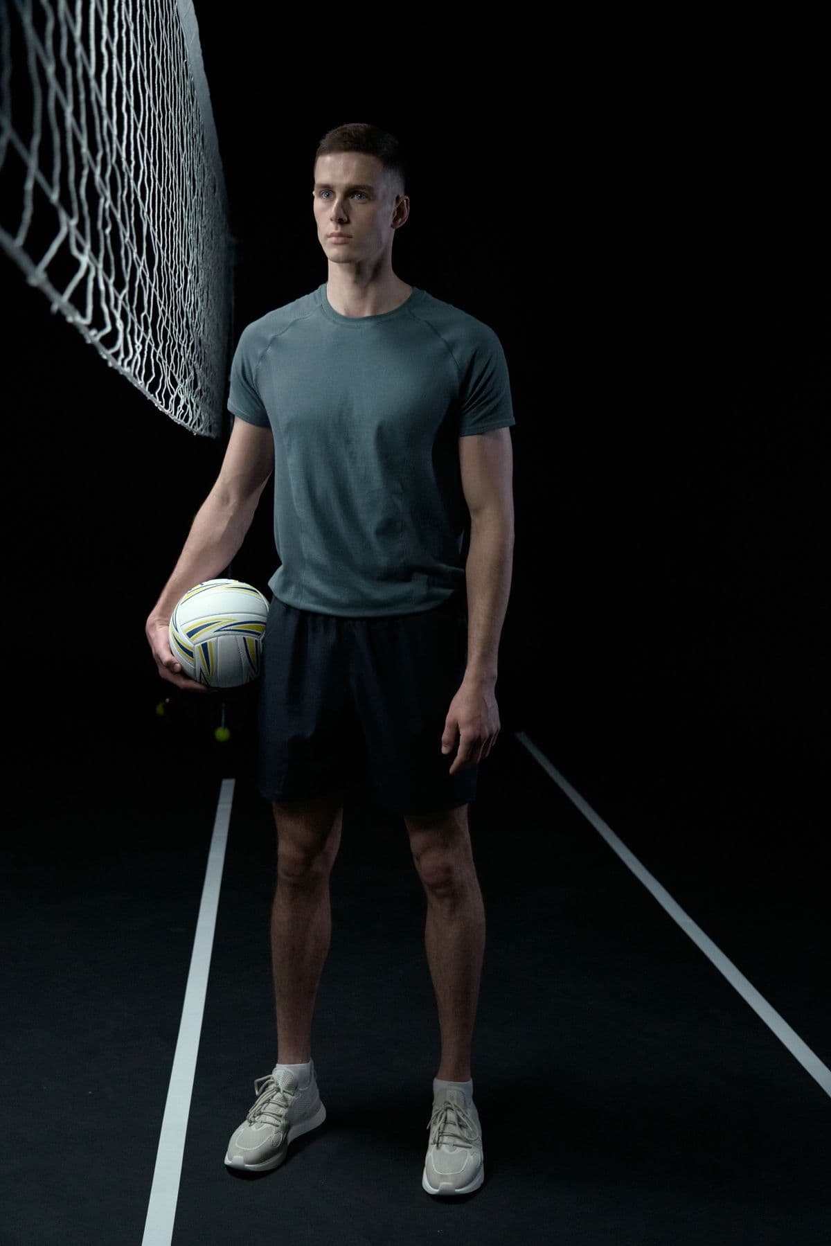 Atleta con un balón de voleibol junto a la red, en un estudio oscuro